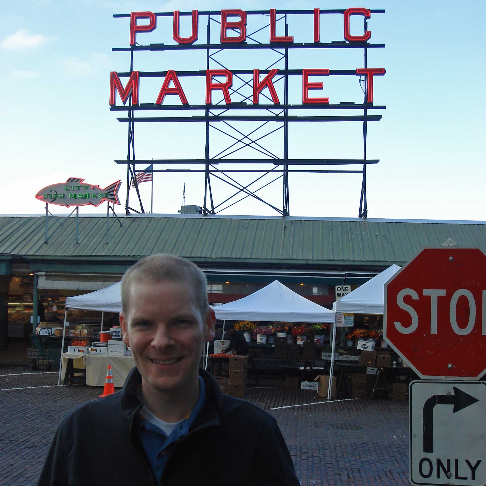 William stand on the street with a large sign in the background that reads
“Public Market”