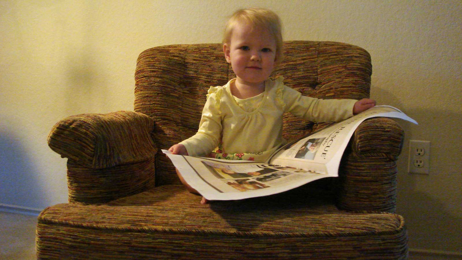 Emily sitting in a chair reading a newspaper